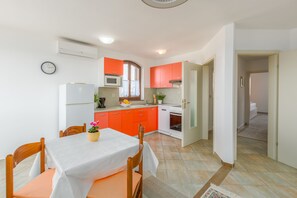 A compact kitchen with a dining area, white walls, and orange cabinets.
