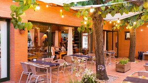 Un café al aire libre con paredes de ladrillo, mesas, sillas y luces colgantes.