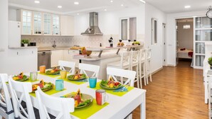 Una cocina moderna con armarios blancos, una isla central y una zona de comedor con sillas blancas y camino de mesa verde.