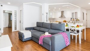 Una sala de estar moderna con un sofá gris, una mesa de comedor con sillas y una cocina al fondo.