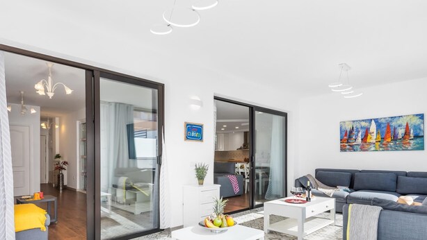 Una sala de estar moderna con un sofá gris, una mesa de centro blanca y un comedor con mesa y sillas.
