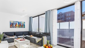Una sala de estar moderna con un sofá seccional gris, mesas de centro blancas y un amplio ventanal con cortinas.