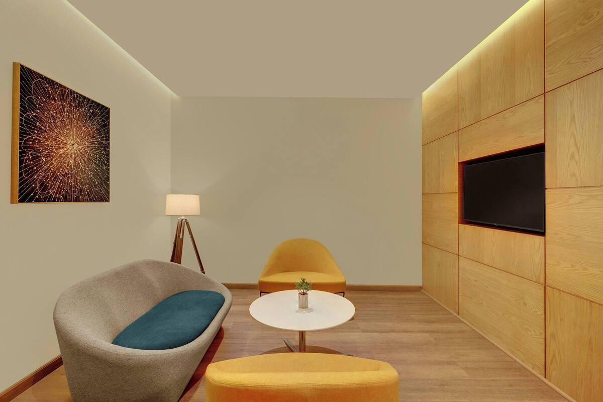 A modern living room with a sofa, armchair, round table, and a flat-screen TV mounted on a wooden panel wall.