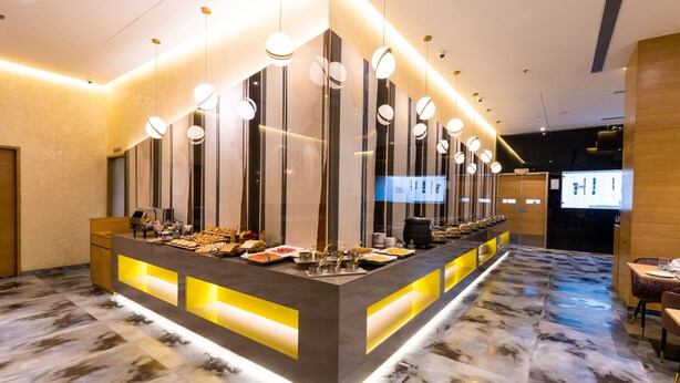 A modern hotel lobby with a central buffet area featuring a variety of food items, a marble floor, and contemporary lighting fixtures. - The Fern Residency Jamnagar, Series by Marriott (Jamnagar)