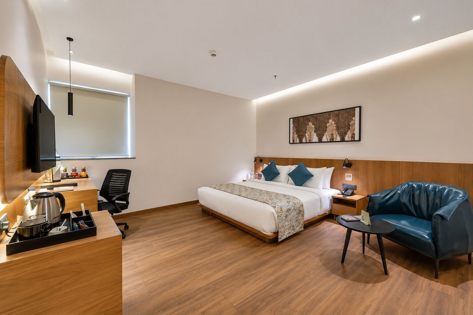 A hotel room with a bed, a desk with a computer, a chair, a sofa, and a television.