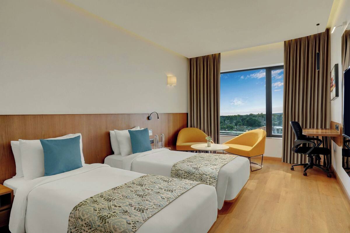 A hotel room with two beds, a small table, a chair, and a desk.