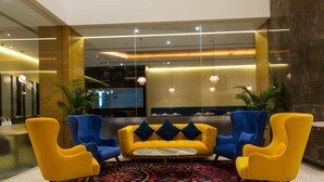 A lobby with a yellow sofa, blue armchairs, and a patterned rug. - The Fern Residency Jamnagar, Series by Marriott (Jamnagar)