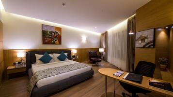 A hotel room with a bed, bedside tables, a desk, a chair, and artwork on the walls.