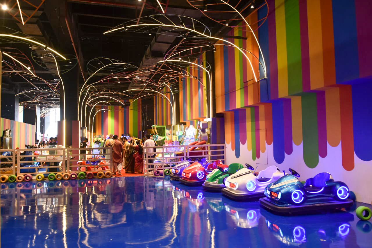 Un espace de jeux intérieur avec des autos tamponneuses et des rayures verticales colorées sur les murs.