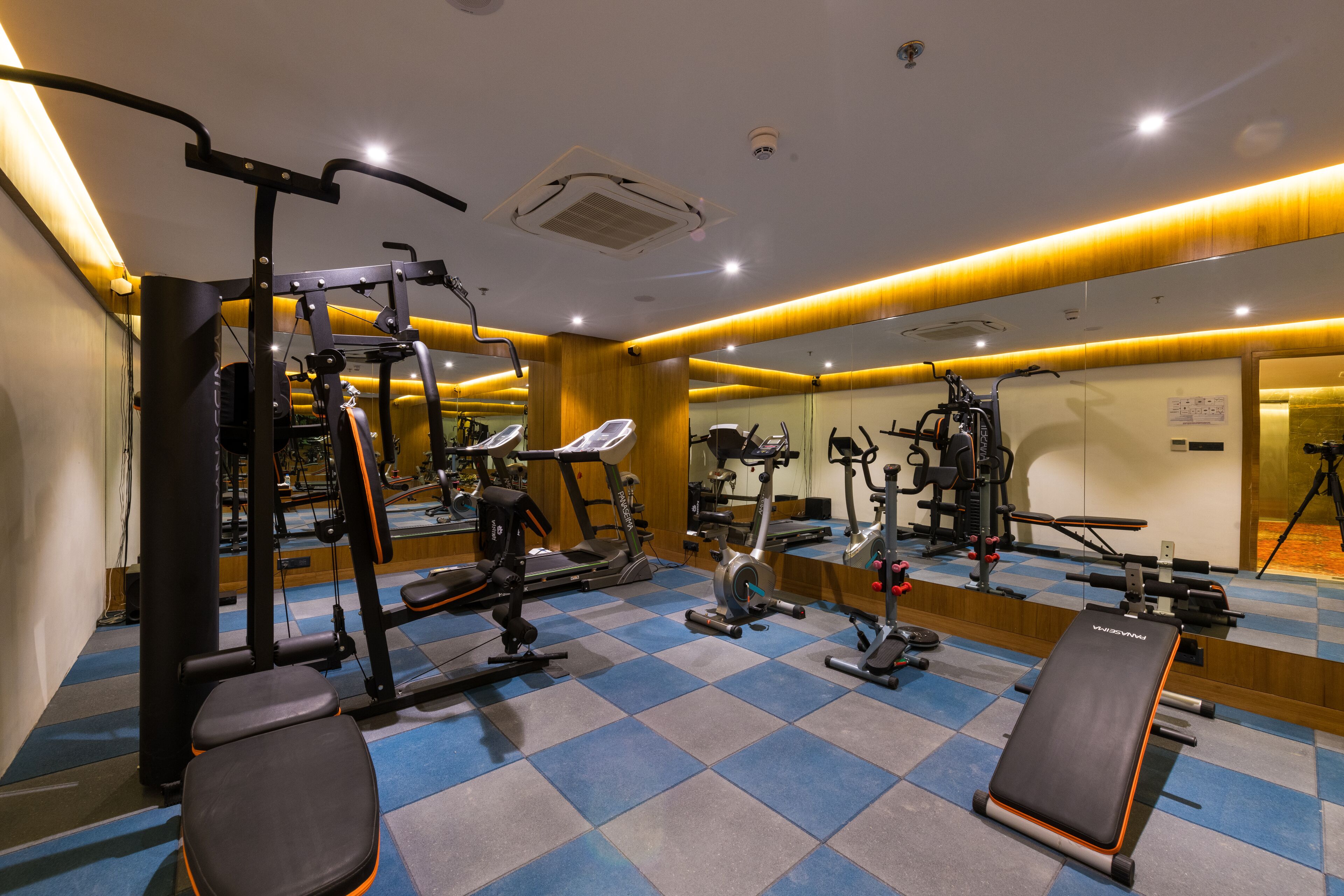 A gym with various exercise equipment, a bench, and a mirrored wall.