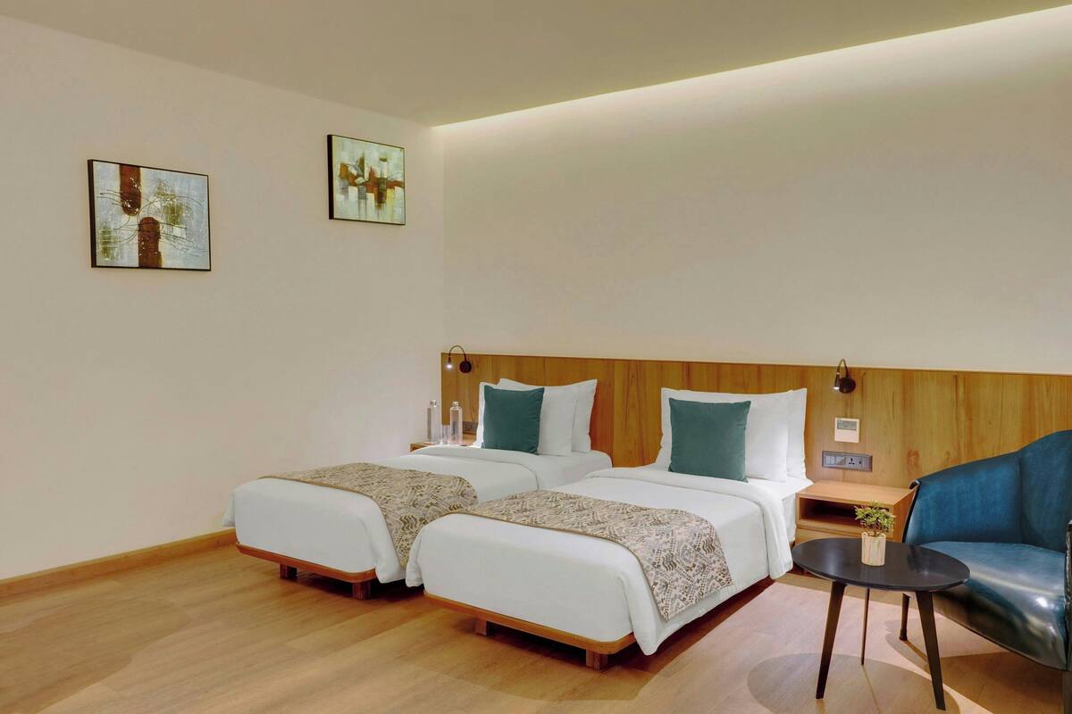 A hotel room with two beds, a wooden headboard, a small table with a plant, and two wall-mounted lamps.