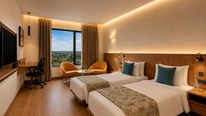 A hotel room with two beds, a desk, a chair, a TV, and a view of the city. - The Fern Residency Jamnagar, Series by Marriott (Jamnagar)
