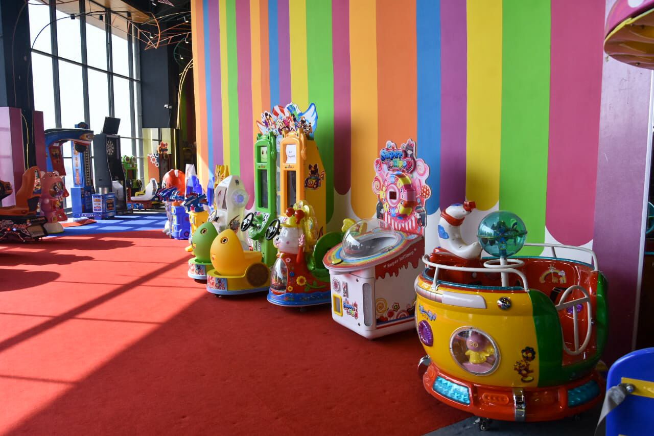 A row of colorful children's ride-on toys against a striped wall.