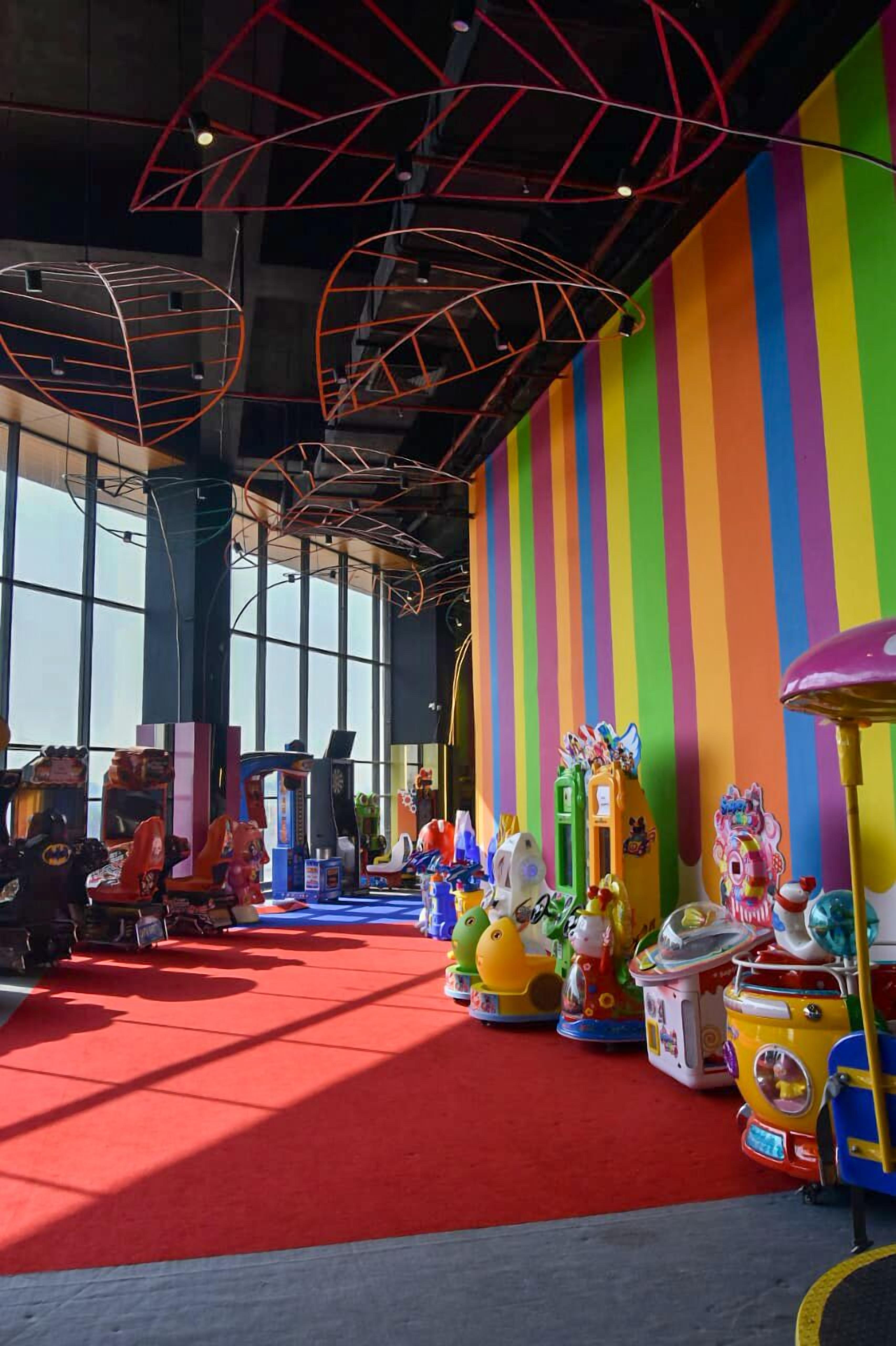 A brightly lit indoor space with colorful striped walls, various arcade games, and a red carpeted floor.