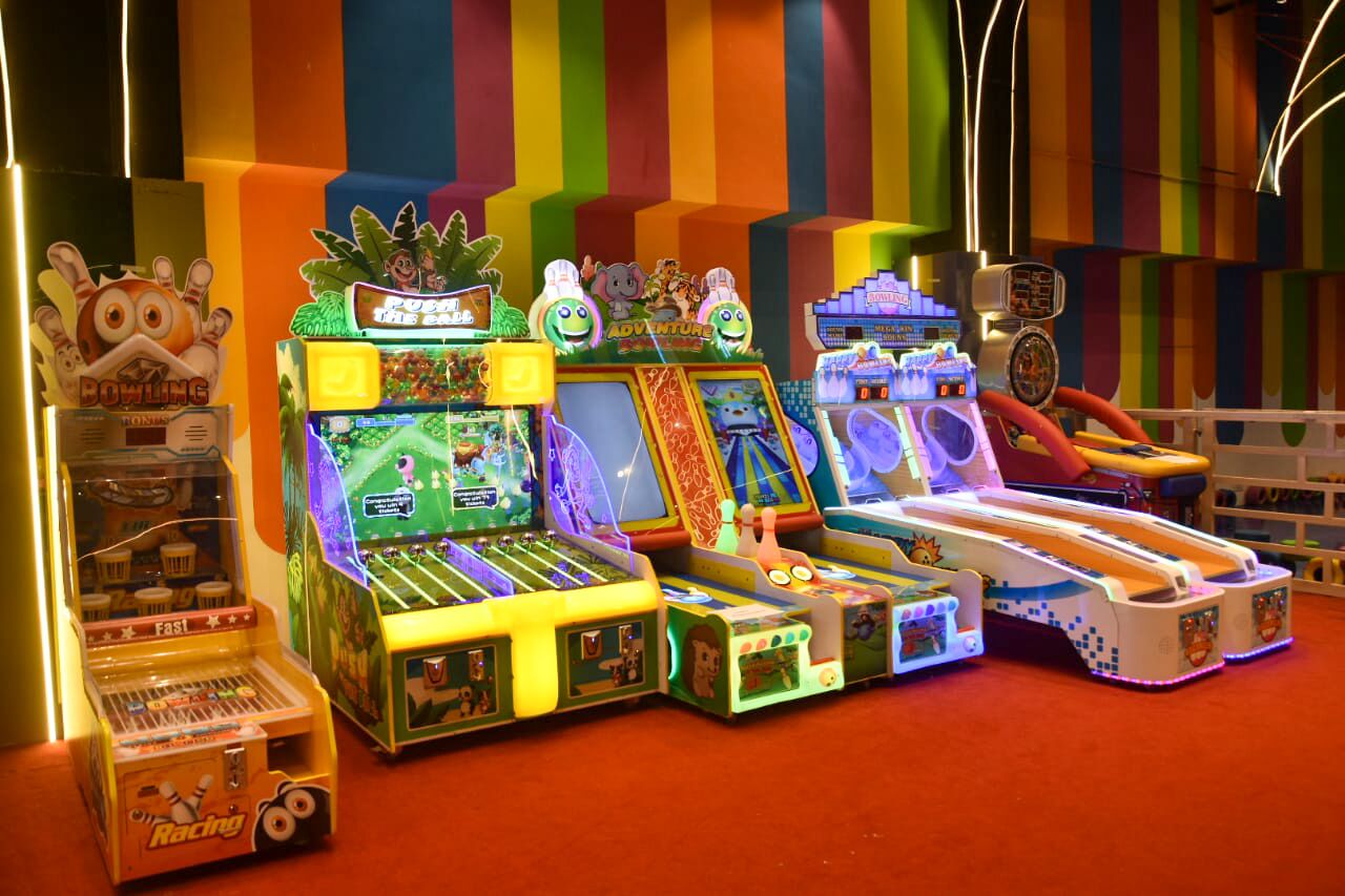 A row of brightly lit arcade machines with various games, including bowling and racing, in a colorful indoor setting.