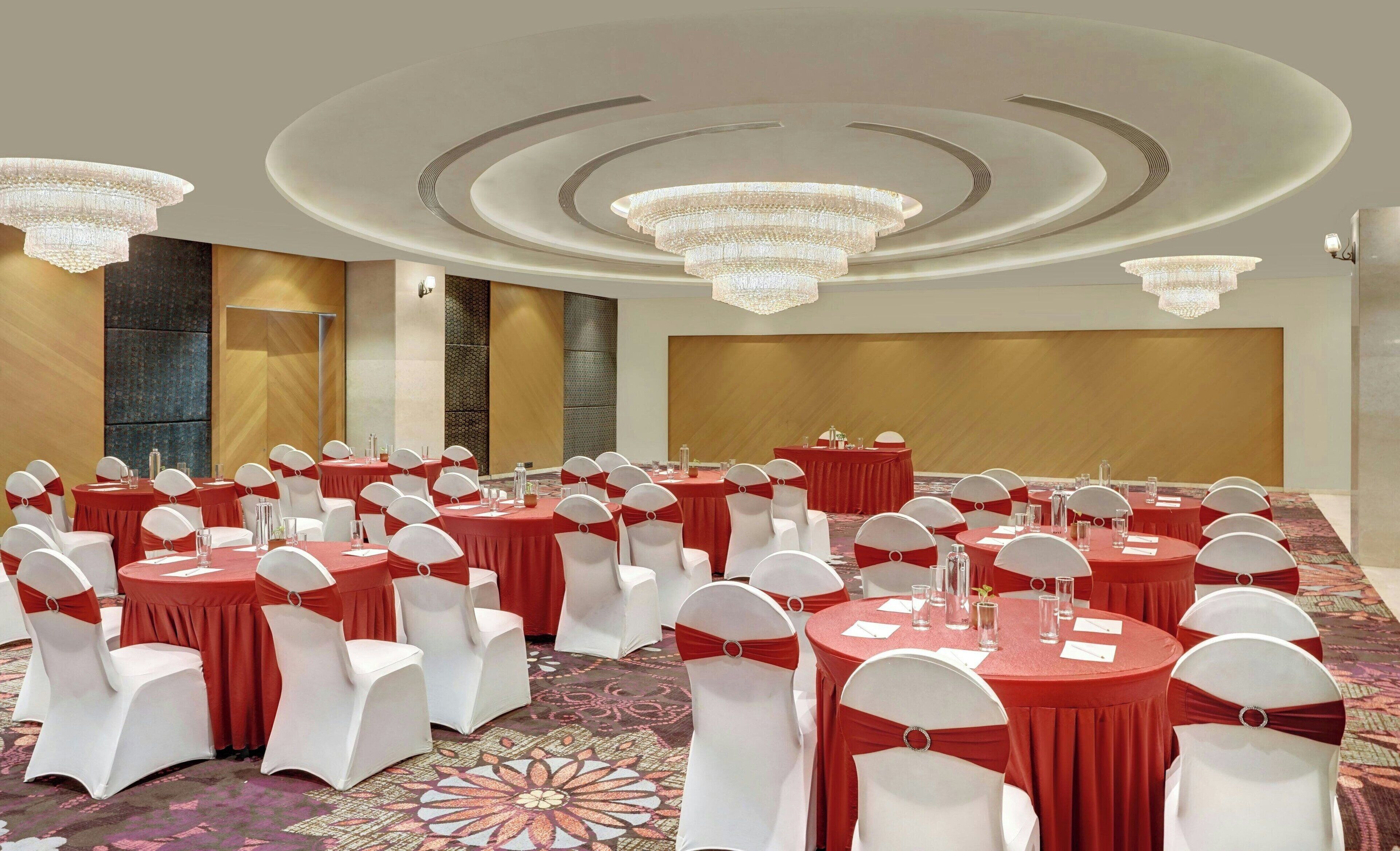 A conference room with round tables, white chairs with red sashes, and chandeliers.