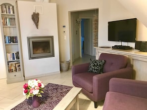 Uma sala de estar com lareira, estante de livros, televisão de tela plana e poltrona roxa.