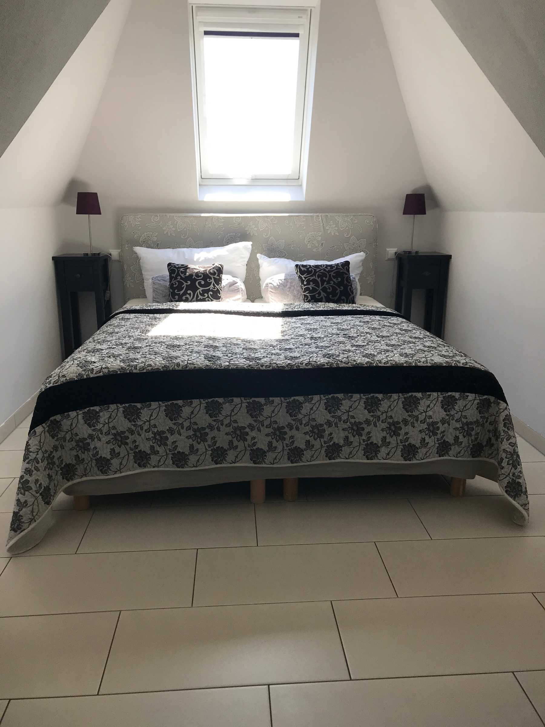 A bedroom with a bed, two nightstands, a window, and a ceiling with a skylight.