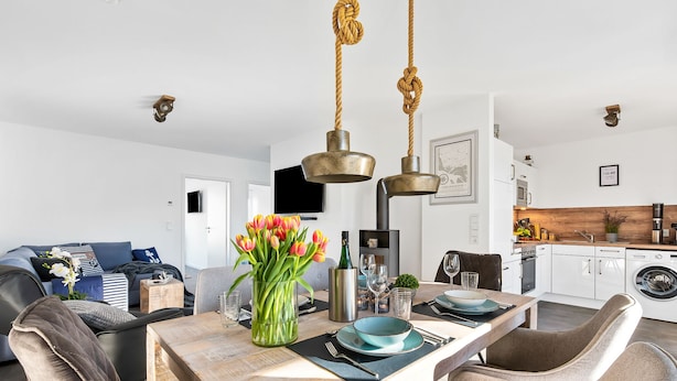 A modern kitchen with a dining area, a sofa set, and a TV in the background.