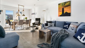 A modern living room with a blue sofa, a wooden coffee table, and a dining area with a table and chairs.