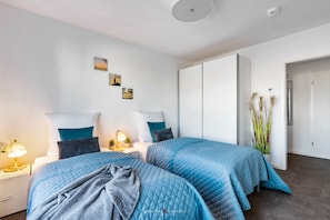 Une chambre avec deux lits, une table de chevet avec une lampe, une plante en pot et une armoire.