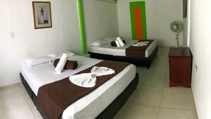 A hotel room with two beds, each with white and brown linens, pillows, and towels. There is a green accent wall, a framed picture on the wall, and a small wooden cabinet.