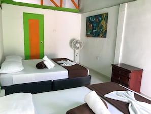 A hotel room with two beds, a green and orange door, a white wall with a painting, and a wooden dresser. - Room with 2 double beds Number 7 (COMBIA)