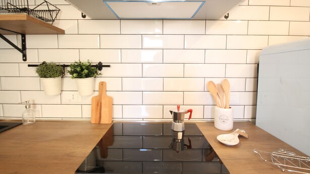 A modern kitchen with a black induction cooktop, white tiled backsplash, wooden cutting board, and a coffee maker.