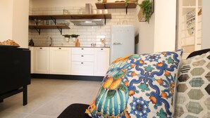 A modern kitchen with white cabinets, a black refrigerator, and a colorful decorative pillow on the sofa.