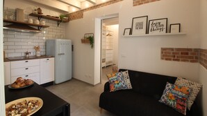 A compact kitchen with white cabinets, a blue refrigerator, and a dining area with a black table and a bowl of food.