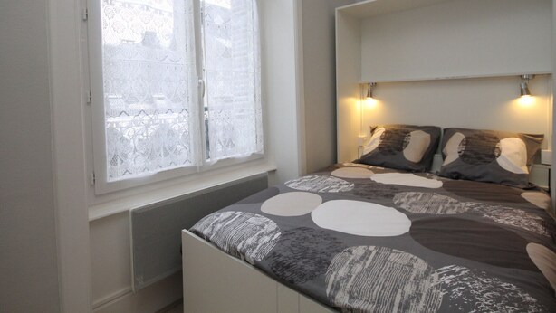 A bedroom with a large window, a bed with a patterned bedspread, and two wall-mounted lamps. - Renovated studio in Mont-Dore center with wifi (Mont-Dore)