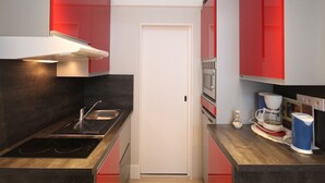 A compact kitchen with red cabinets, a white door, a microwave, a coffee maker, and a stove. - Renovated studio in Mont-Dore center with wifi (Mont-Dore)