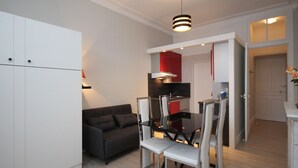 A compact living space with a kitchenette, a dining area with a table and chairs, a sofa, and a ceiling light fixture. - Renovated studio in Mont-Dore center with wifi (Mont-Dore)