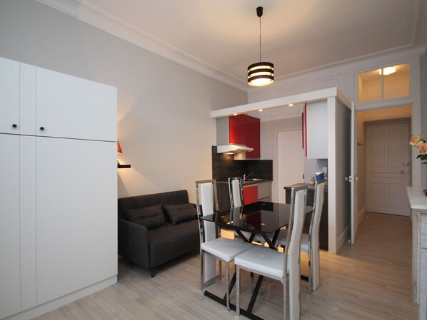 A compact living space with a kitchenette, a dining area with a table and chairs, a sofa, and a ceiling light fixture.