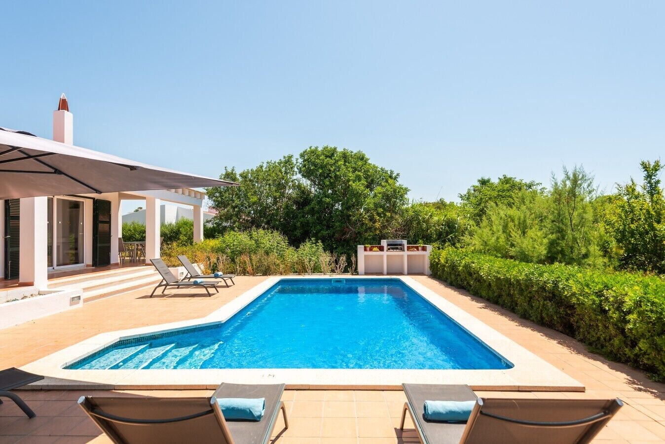 Uma piscina retangular com superfície de água azul cristalina, ladeada por um deck revestido de azulejos.