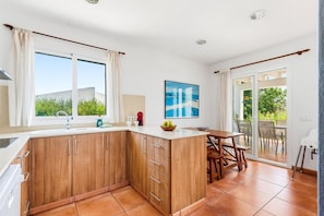 A modern kitchen with wooden cabinets, a built-in island, and a dining area with a table and chairs. - Villa Casa Nova, Piscina, Wifi, AC gratis (Sant Lluís)