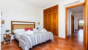 Quarto com cabeceira de madeira, cama com roupa de cama listrada, mesa de cabeceira com uma planta e guarda-roupa de madeira.