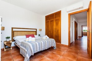 A bedroom with a wooden headboard, a bed with striped bedding, a nightstand with a plant, and a wooden wardrobe. - Villa Casa Nova, Piscina, Wifi, AC gratis (Sant Lluís)