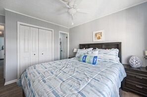 Een slaapkamer met een bed, een plafondventilator, een dressoir en een wandlamp.