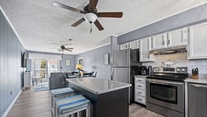 A modern kitchen with stainless steel appliances, a central island, and a ceiling fan. - Sea Robin 207 by Seaside Vacations & Sales (Ocean City)