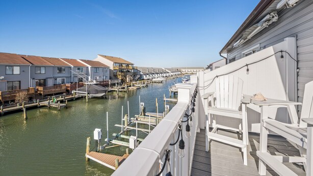 A marina with docked boats, a wooden deck, and a row of houses along the water. - Sea Robin 207 by Seaside Vacations & Sales (Ocean City)
