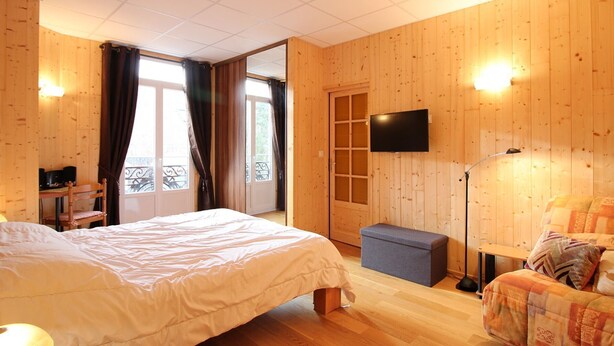 Ein Schlafzimmer mit einem Bett, einem Schreibtisch, einem Stuhl, einem Fernseher und einem Balkon.