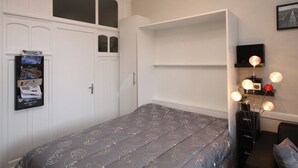 Un dormitorio con cama, armario, estantería y escritorio con lámpara.