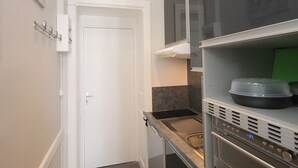 Cocina estrecha con una puerta blanca, campana de acero inoxidable y microondas sobre una encimera.
