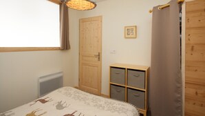 Une chambre à coucher comprenant un lit, une armoire en bois, une table de chevet, un luminaire suspendu et une fenêtre avec des rideaux.