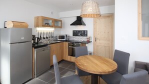 Une cuisine compacte dotée d’appareils électroménagers modernes, un coin repas avec une table et des chaises en bois, et un luminaire suspendu.