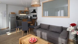 Un appartement moderne avec un canapé gris, une table à manger en bois et un coin cuisine équipé d’un réfrigérateur, d’un four à micro-ondes et d’un évier.