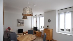 Un salon moderne avec une table de salle à manger ronde en bois, des chaises bleues, un canapé gris, un téléviseur et un meuble en bois.