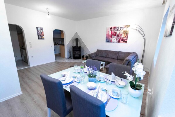 Un coin repas avec une table dressée pour quatre personnes, un canapé et une cheminée en arrière-plan.