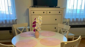 A dining area with a round table, white chairs, pink placemats, and a vase with flowers. - Studio mit Garten - Casa Lauda in Bad Vöslau (Bad Vöslau)